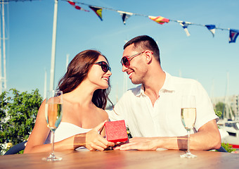 Image showing smiling couple with champagne and gift at cafe