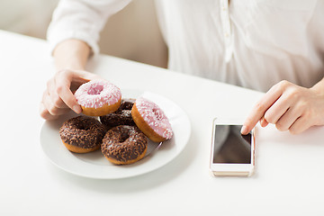 Image showing close up of hands with smart phone and donuts