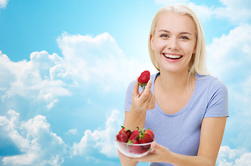 Image showing happy woman eating strawberry over sky