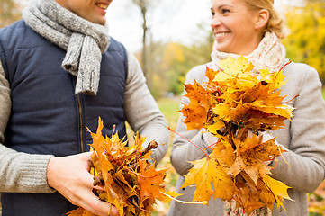 Image showing smiling couple with maple leaves in autumn park