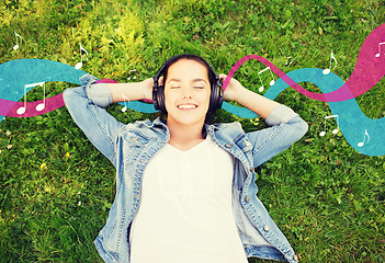 Image showing smiling young girl in headphones lying on grass