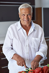 Image showing senior man cooking at home preparing salad in kitchen