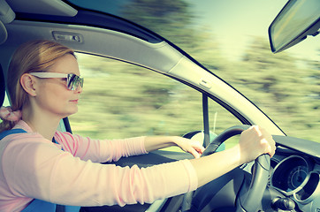 Image showing Pretty woman in sunglasses driving fast car filtered and toned