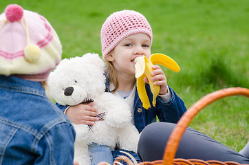 Image showing Girl on picnic eats a banana and holds bear