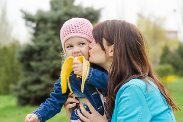 Image showing Mom kisses the girl who eats a banana on picnic