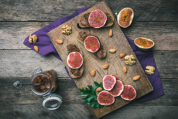 Image showing Sliced figs, nuts and bread with jam on choppingboard in rustic 