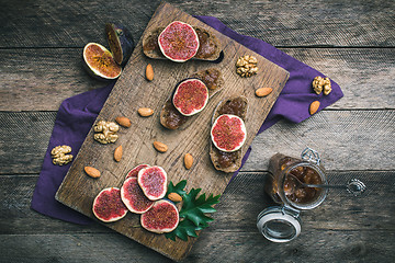 Image showing Cut figs, nuts and bread with jam on choppingboard in rustic sty