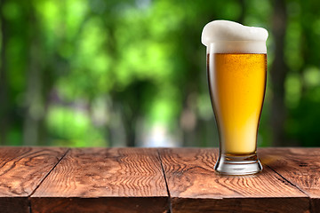 Image showing Beer in glass on wooden table against green