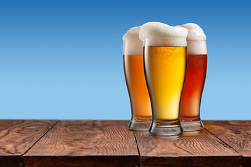 Image showing Different beer in glasses on wooden table and blue background