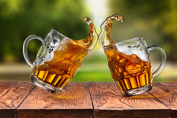 Image showing Splash of beer in two glasses on wooden table against park