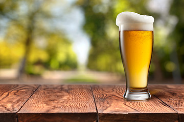 Image showing Beer in glass on wooden table against green