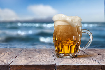 Image showing Glass of beer on wooden table with sea on background