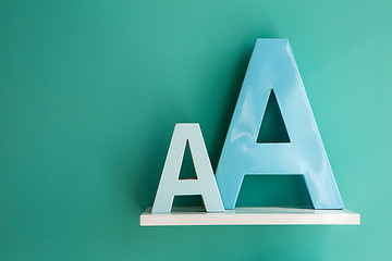 Image showing Letters A small and big size turquoise color on a white shelf.