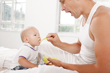 Image showing Young father with his nine months old son on the bed at home