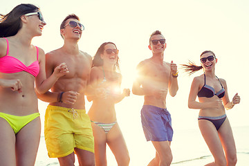 Image showing smiling friends in sunglasses running on beach