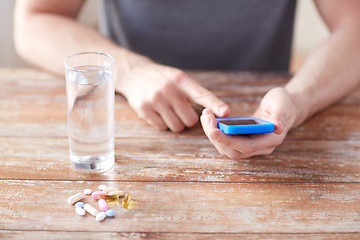 Image showing close up of hands with smartphone, pills and water