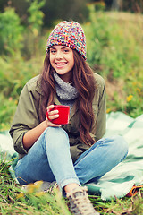 Image showing smiling young woman with cup sitting in camping