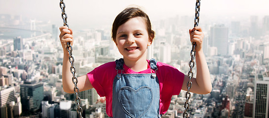 Image showing happy little girl swinging on swing over city