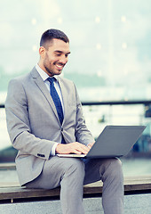 Image showing smiling businessman working with laptop outdoors