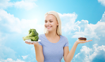 Image showing smiling woman with broccoli and donut over sky