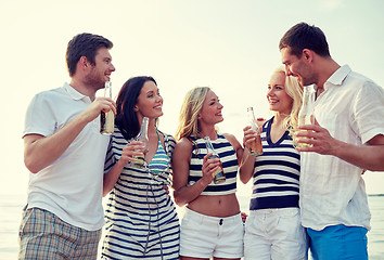 Image showing smiling friends with drinks in bottles on beach