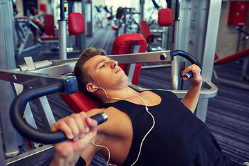 Image showing young man with earphones exercising on gym machine