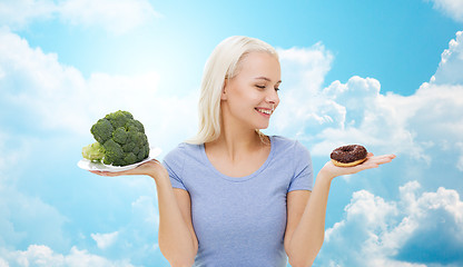 Image showing smiling woman with broccoli and donut over sky