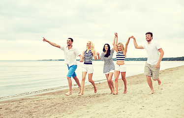 Image showing smiling friends in sunglasses running on beach