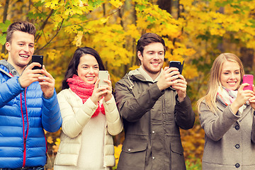 Image showing smiling friends with smartphones in city park