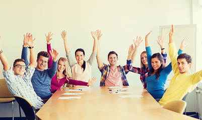 Image showing group of smiling students raising hands in office