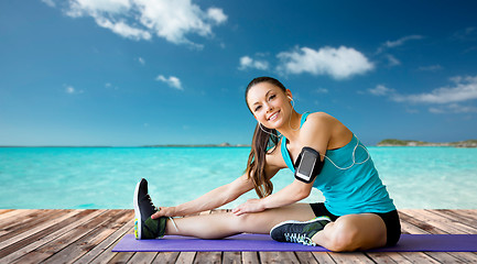 Image showing smiling woman stretching leg on mat over sea