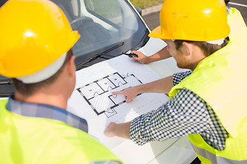 Image showing close up of builders with blueprint on car hood