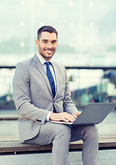 Image showing smiling businessman working with laptop outdoors