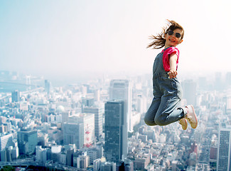 Image showing happy little girl jumping over city background