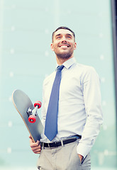 Image showing young smiling businessman with skateboard outdoors