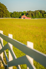 Image showing  white fence leading up to a big red barn