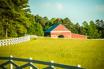 Image showing  white fence leading up to a big red barn