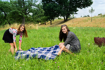 Image showing Two girls  spreading a blanket for picnic