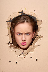 Image showing Displeased woman peeping through hole in paper