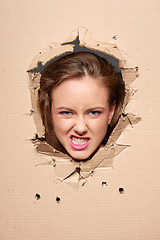 Image showing Displeased girl peeping through hole in paper