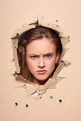 Image showing Displeased girl peeping through hole in paper