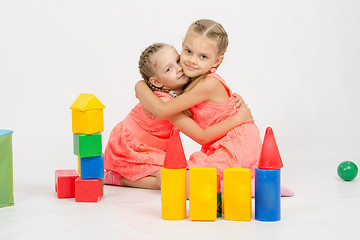 Image showing Happy two girls embrace building a castle out of blocks