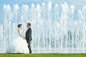 Image showing Bride and groom holding hands in front of water fountain