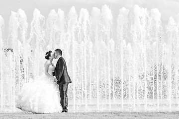 Image showing Bride and groom kissing in front of water fountain black and whi