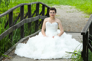 Image showing Bride sitting on wooden bridge