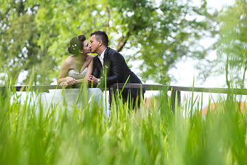 Image showing Newlyweds kissing on wooden bridge