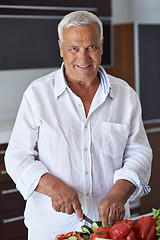 Image showing senior man cooking at home preparing salad in kitchen