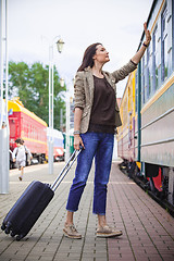 Image showing woman with luggage waves his hand near passenger railcar 