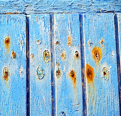 Image showing stripped paint in the blue wood door and rusty nail