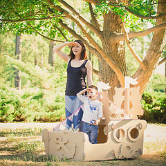 Image showing Mom and child playing in a cardboard boat. Summer day.